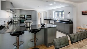 A modern kitchen with a central island, bar stools, and a dining area with a wooden table and cushioned chairs. - 6 bedroom accommodation in Howell (Howell)