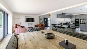 A modern kitchen with a central island, built-in appliances, and a dining area with a wooden table and cushioned seating. - 6 bedroom accommodation in Howell (Howell)
