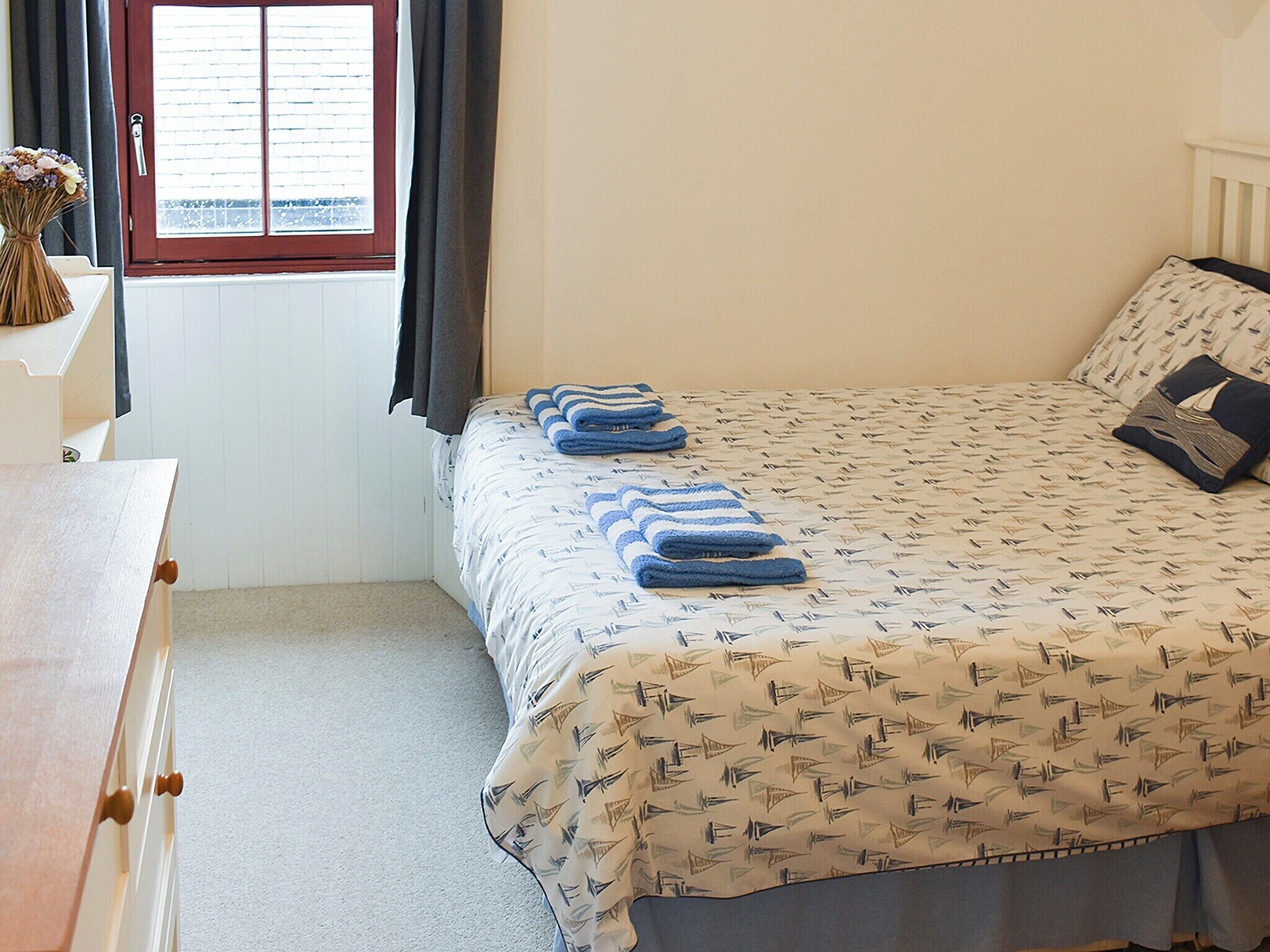 A bedroom with a bed, a window with curtains, a dresser, and a radiator.