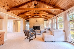 A spacious living room with a stone fireplace, wooden ceiling beams, and large windows. - Waterfront Escape Near Annapolis (Edgewater)