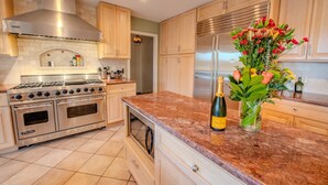 Cocina con estufa Viking, campana extractora de acero inoxidable, gabinetes de madera, encimera de mármol y un florero con flores.