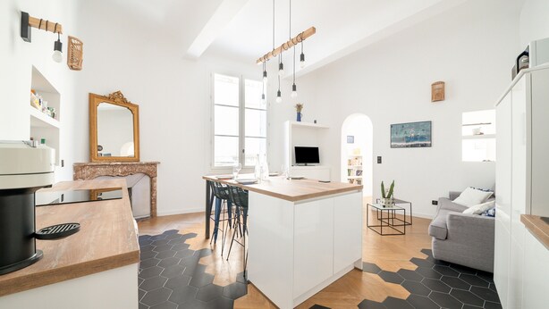 A modern kitchen with a central island, bar stools, and a dining area with a grey sofa. - Le Saint Firmin - Two Bedroom Apartment, Sleeps 4 (Montpellier)