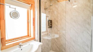 Ein modernes Badezimmer mit Marmorwand, einer Glasdusche, einem Waschbecken inklusive Spiegel und einem Fenster mit Jalousien.