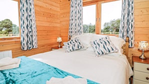 Ein Schlafzimmer einer Holzhütte mit Bett, Kissen, einem Nachttisch und einem Fenster mit Vorhängen.