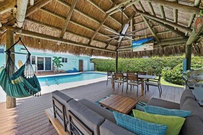 Un espace extérieur abrité, doté d’une piscine, de sièges et d’un toit de chaume.