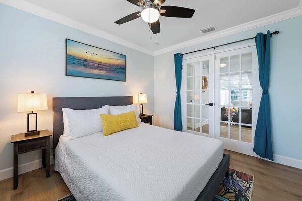 A bedroom with a bed, two bedside lamps, a ceiling fan, a window with curtains, and a painting on the wall. - Tiki Paradise! Pool, mini golf, kids’ playhouse, arcade! (Dania Beach)