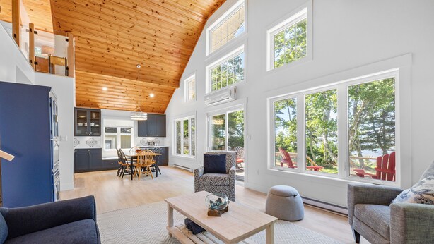 A spacious living area with a high ceiling, large windows, and a view of the outdoors. - Water Front Cottage in Stanley Bridge- Just Minutes To Cavendish Beach (Breadalbane)