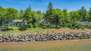 A lakeside property with a stone wall, a dock, and multiple houses surrounded by trees. - Water Front Cottage in Stanley Bridge- Just Minutes To Cavendish Beach (Breadalbane)