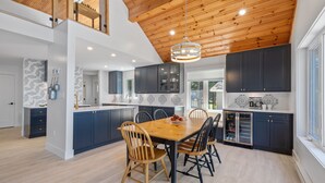 A modern kitchen with dark blue cabinets, a wooden dining table, and a hanging light fixture. - Water Front Cottage in Stanley Bridge- Just Minutes To Cavendish Beach (Breadalbane)