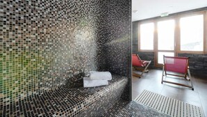 Ein Wellnessraum mit Wand aus Mosaik, einer Sitzbank mit Handtüchern und Blick ins Freie durch große Fenster.