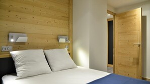 Ein Schlafzimmer mit einem hölzernen Kopfstück, zwei Nachttischlampen, einem Bett mit weißer Bettwäsche und einer Holztür.