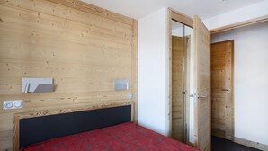 Ein Schlafzimmer mit einem hölzernen Kopfteil, einer roten Bettdecke, einem Nachttisch und einer Tür zu einem anderen Raum.
