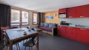 Ein kompaktes Zimmer mit Esstisch, Stühlen, einer Couch und einer Küchenzeile mit roten Schränken.