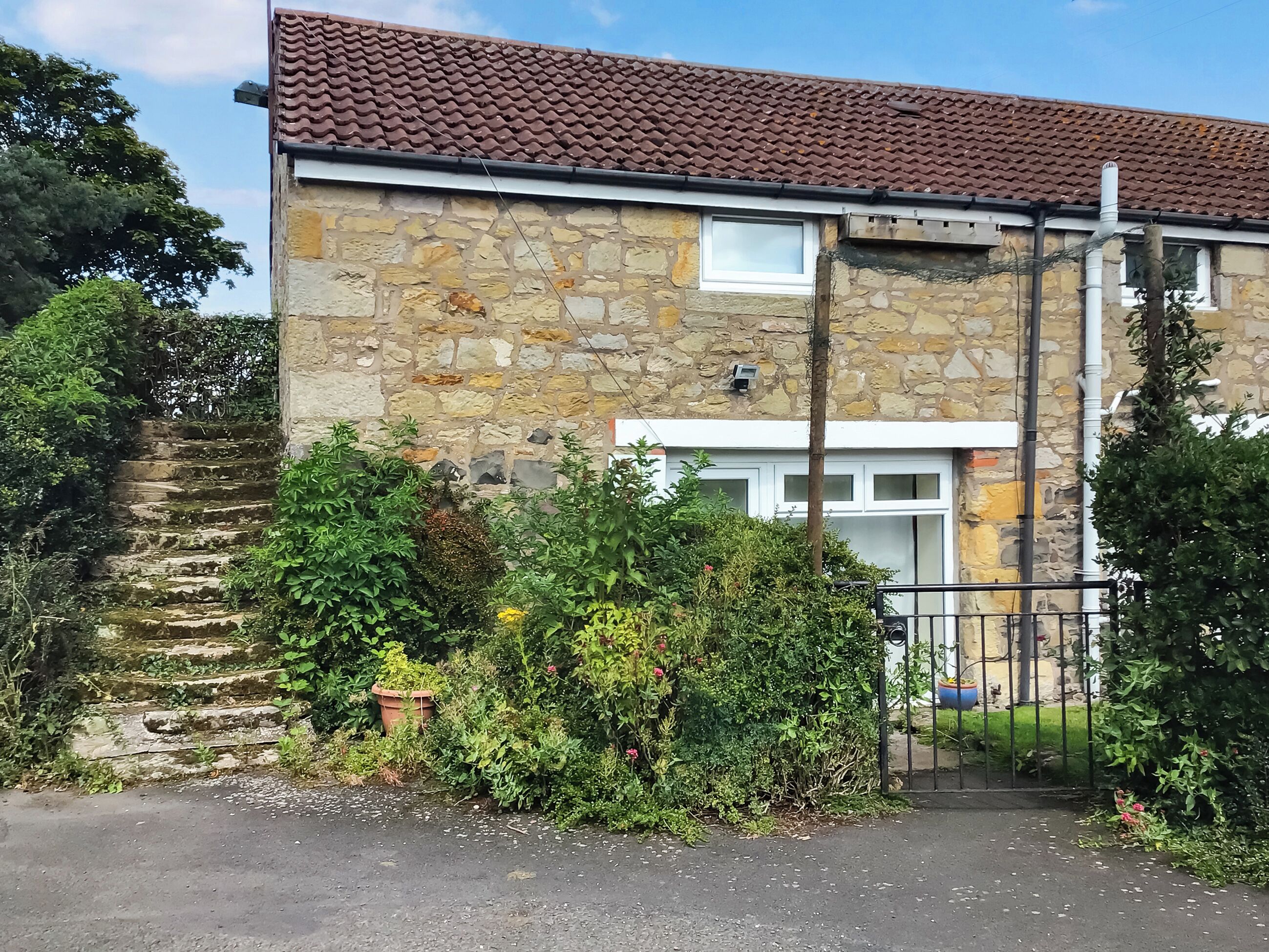 Une maison en pierre avec un toit en tuiles, une entrée fermée par un portail et un escalier menant à une porte.