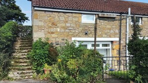 A stone house with a tiled roof, a gated entrance, and a staircase leading to a door.