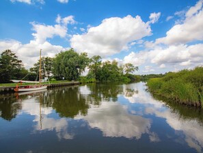 A calm river with a boat docked on the left, surrounded by greenery and trees.