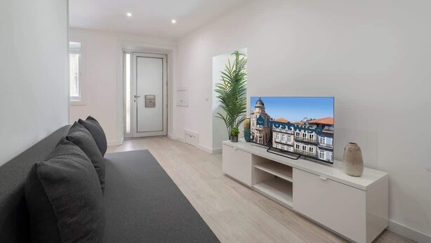 A modern living room with a sofa, a TV on a white stand, and a door leading to another room. - Downtown Cosy House by Host Wise (Porto)