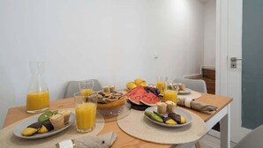 A breakfast table with various fruits, pastries, and orange juice in a modern room with white walls and a door. - Downtown Cosy House by Host Wise (Porto)