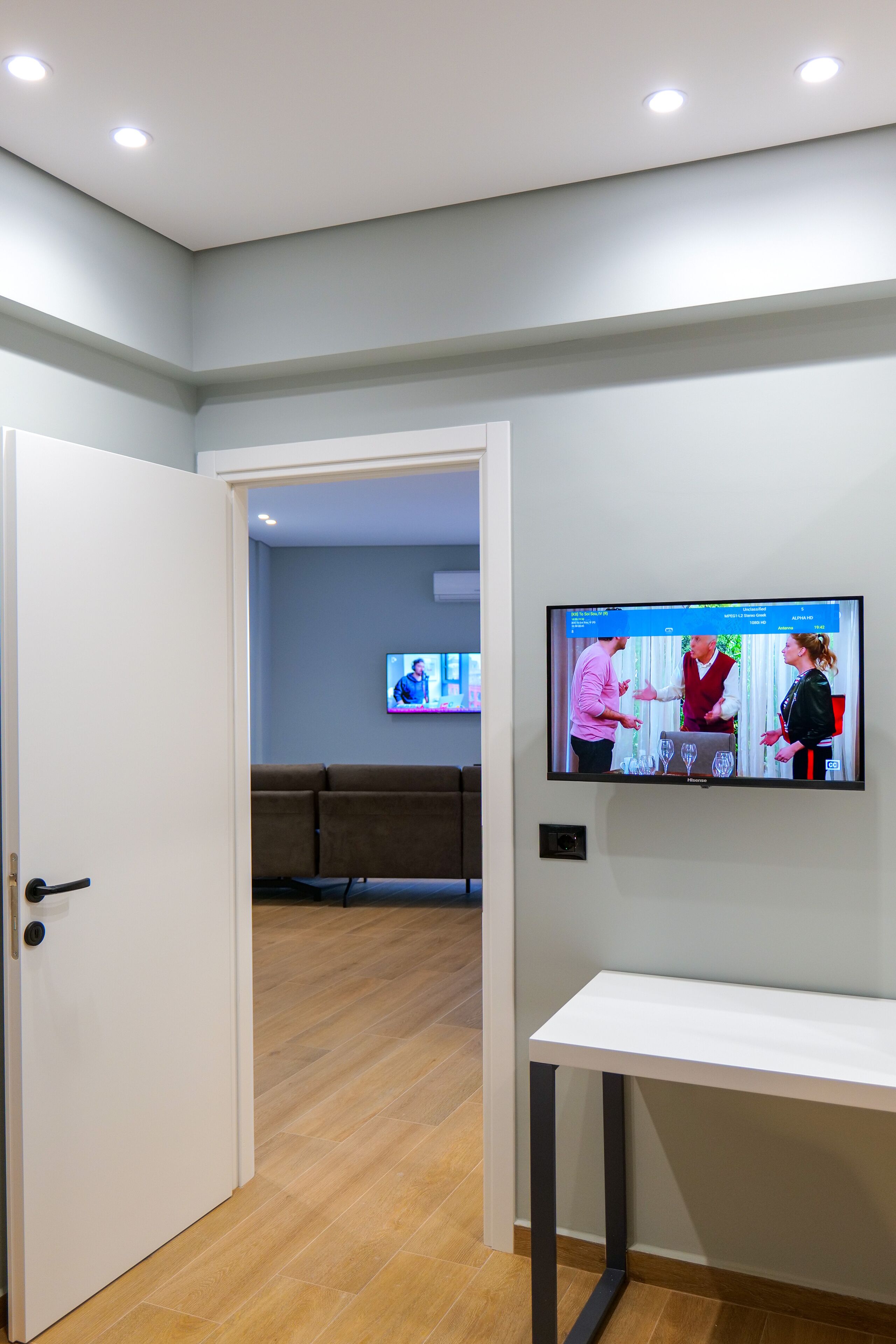 A hotel room with a TV on the wall, a white door, and a wooden floor.