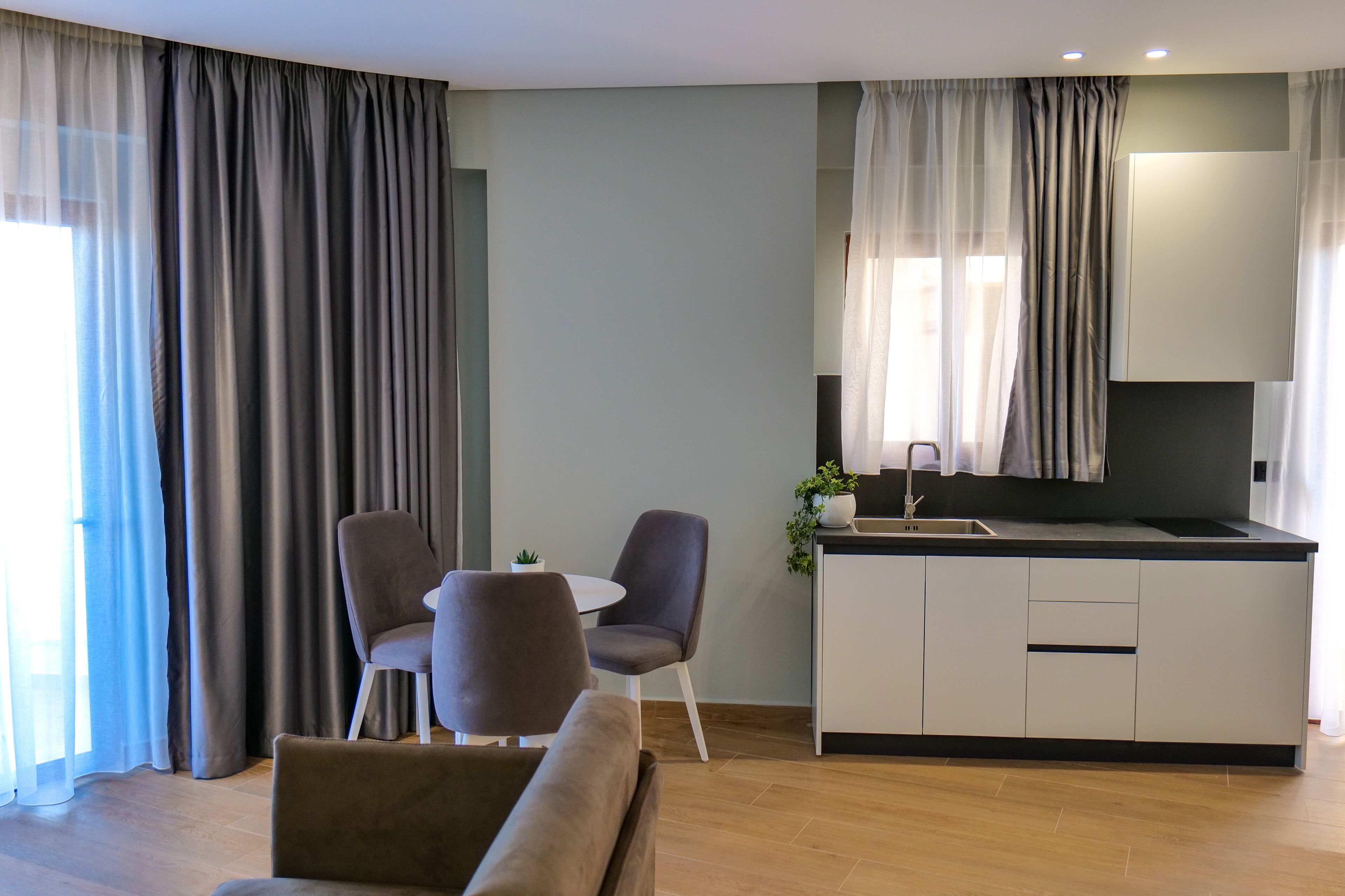 A modern living room with a sofa, two chairs, a small table, and a kitchen area with a counter and cabinets.