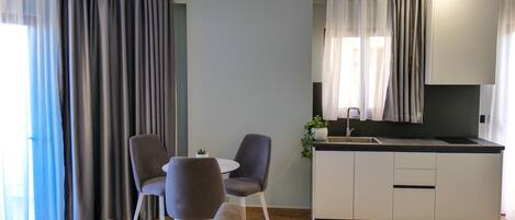 A modern living room with a sofa, two chairs, a small table, and a kitchen area with a counter and cabinets.