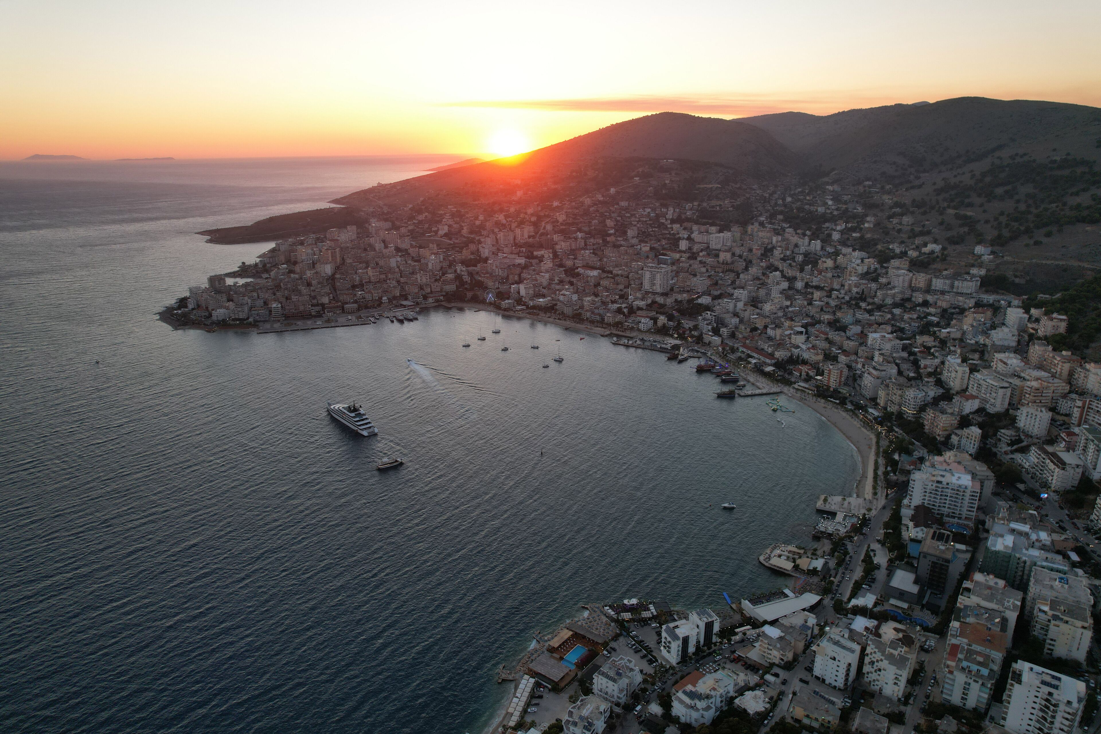 An aerial view of a coastal city with a marina, buildings, and a sunset.