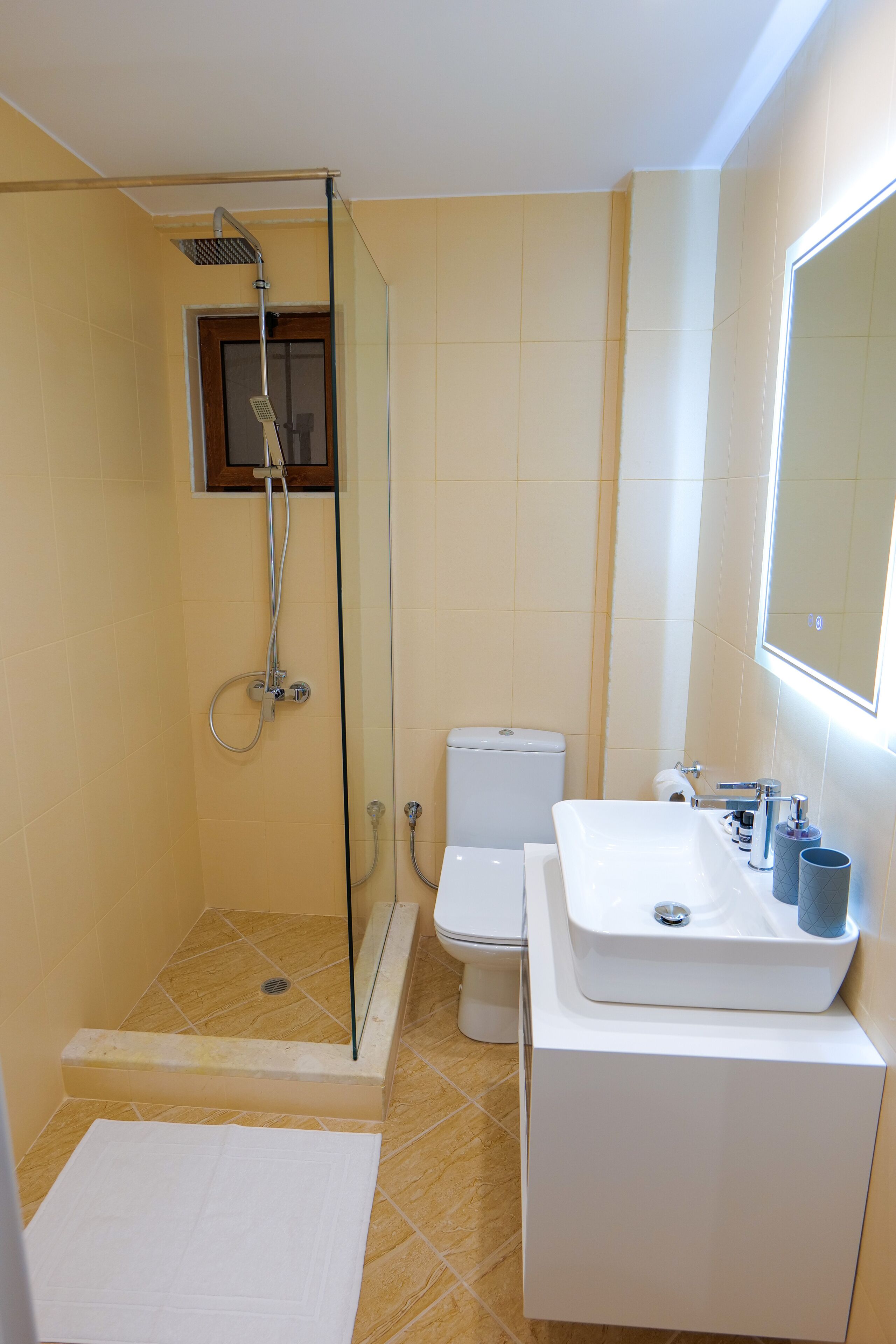 Un baño con ducha envuelta en vidrio, inodoro y lavamanos con espejo superior.