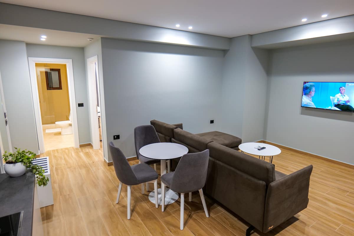 A modern room with a sofa, two chairs, a small round table, and a TV on the wall.