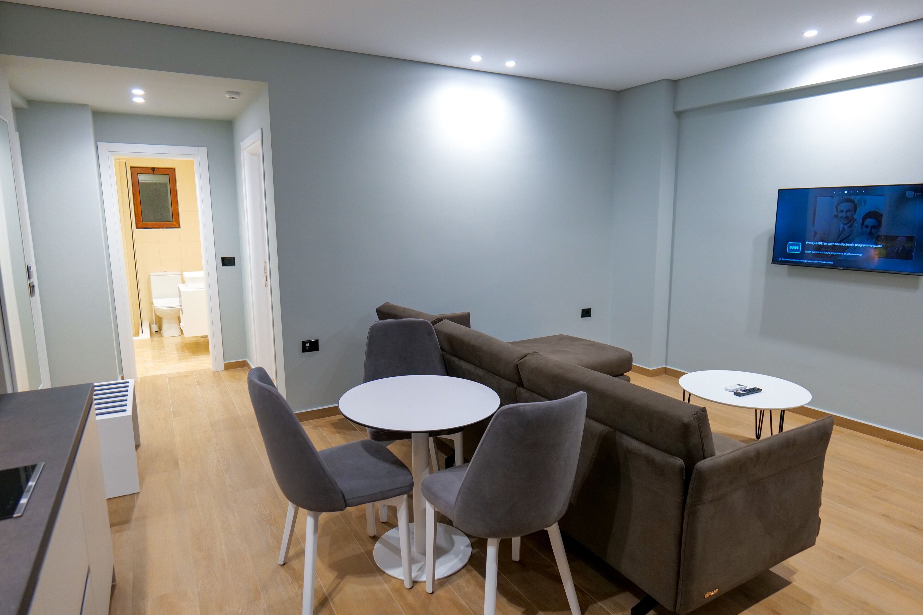 A modern room with a sofa, two chairs, a small table, and a TV mounted on the wall.