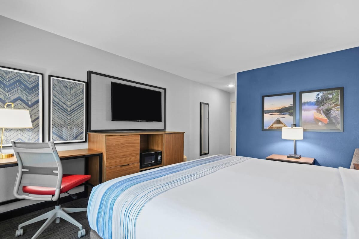 Ein Hotelzimmer mit Bett, Schreibtisch, Stuhl, Fernseher und Bildern an den Wänden.