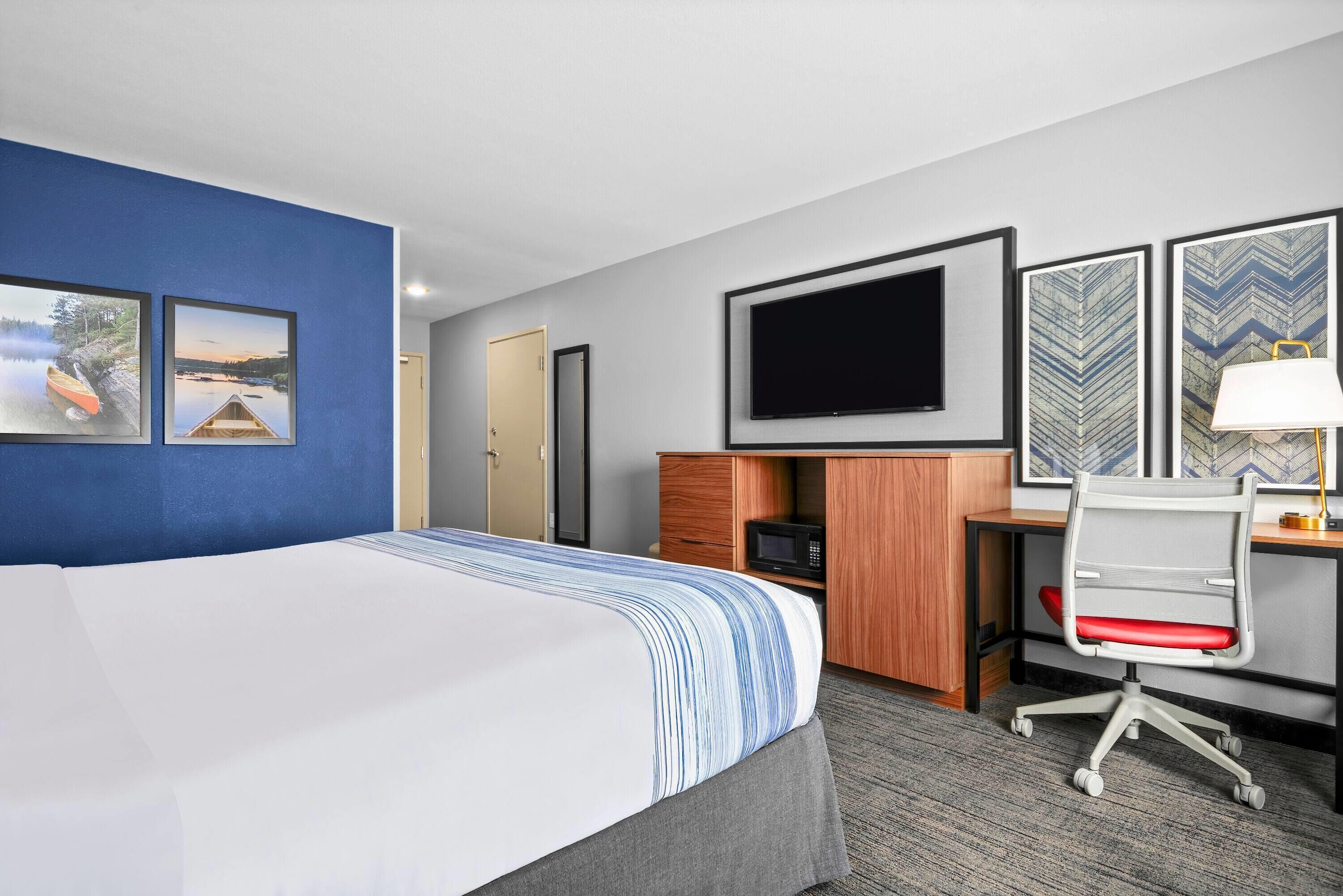 Une chambre d’hôtel avec un grand lit, un bureau avec un ordinateur, une télévision et deux tableaux encadrés au mur.