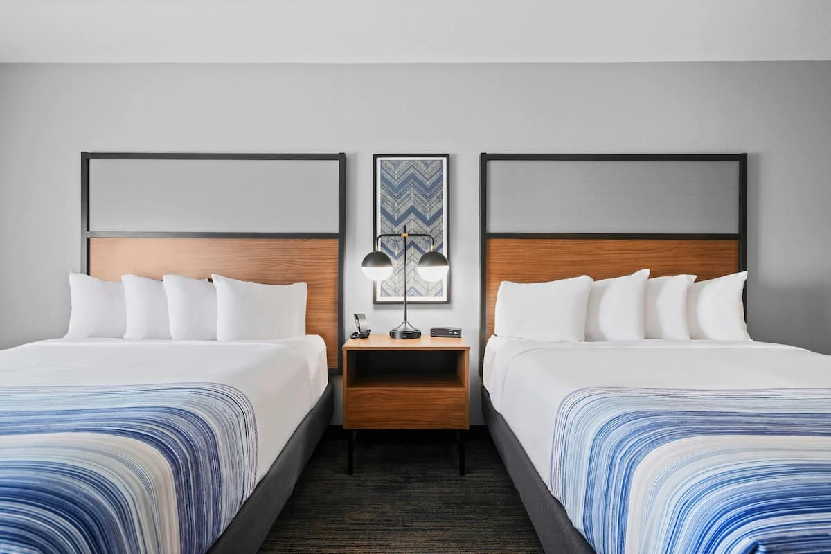 Ein Hotelzimmer mit zwei Betten, einem Nachttisch mit Lampe und einem Wandbild.