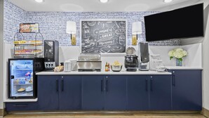 Cozinha equipada com geladeira, cafeteira, torradeira e lousa com itens de café da manhã.
