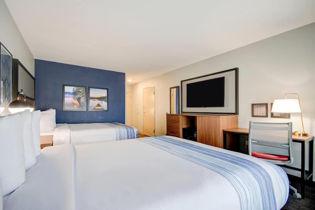 Ein Hotelzimmer mit zwei Betten, einem Fernseher, einem Schreibtisch mit Lampe und einer Tür.