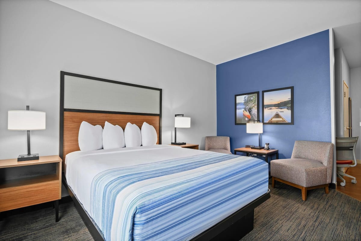 Ein Hotelzimmer mit einem großen Bett, zwei Nachttischen, einem Sessel und einem Schreibtisch mit Lampe.