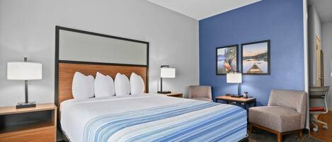 A hotel room with a large bed, two bedside tables, a chair, and a desk with a lamp.