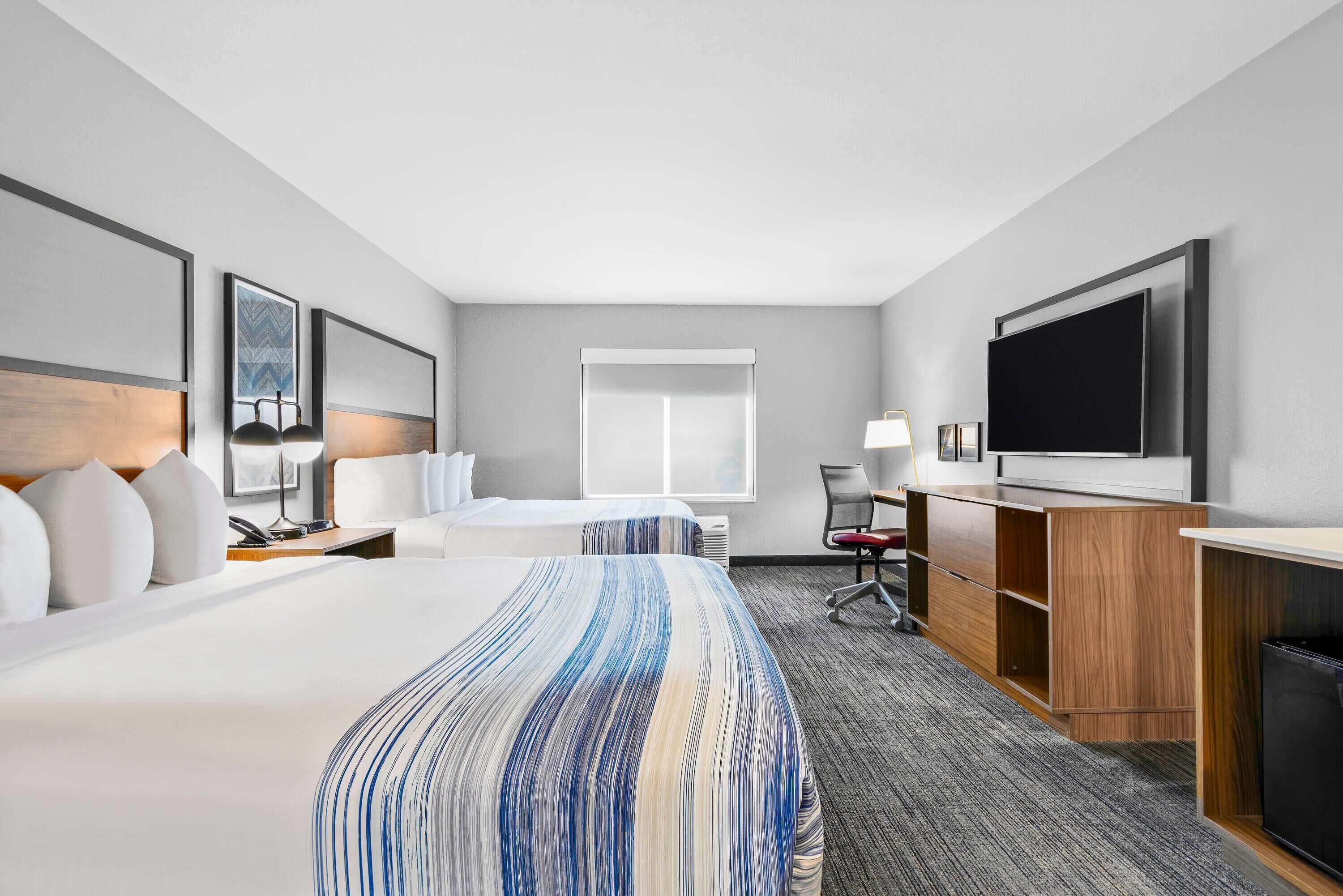 A modern hotel room with a large bed, a desk, a TV, and a window.