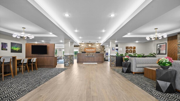 Um hall de hotel moderno com balcão de recepção, área de estar e piso de madeira.