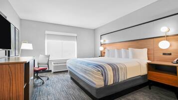 A hotel room with a large bed, a desk, a chair, a TV, and a window with blinds.