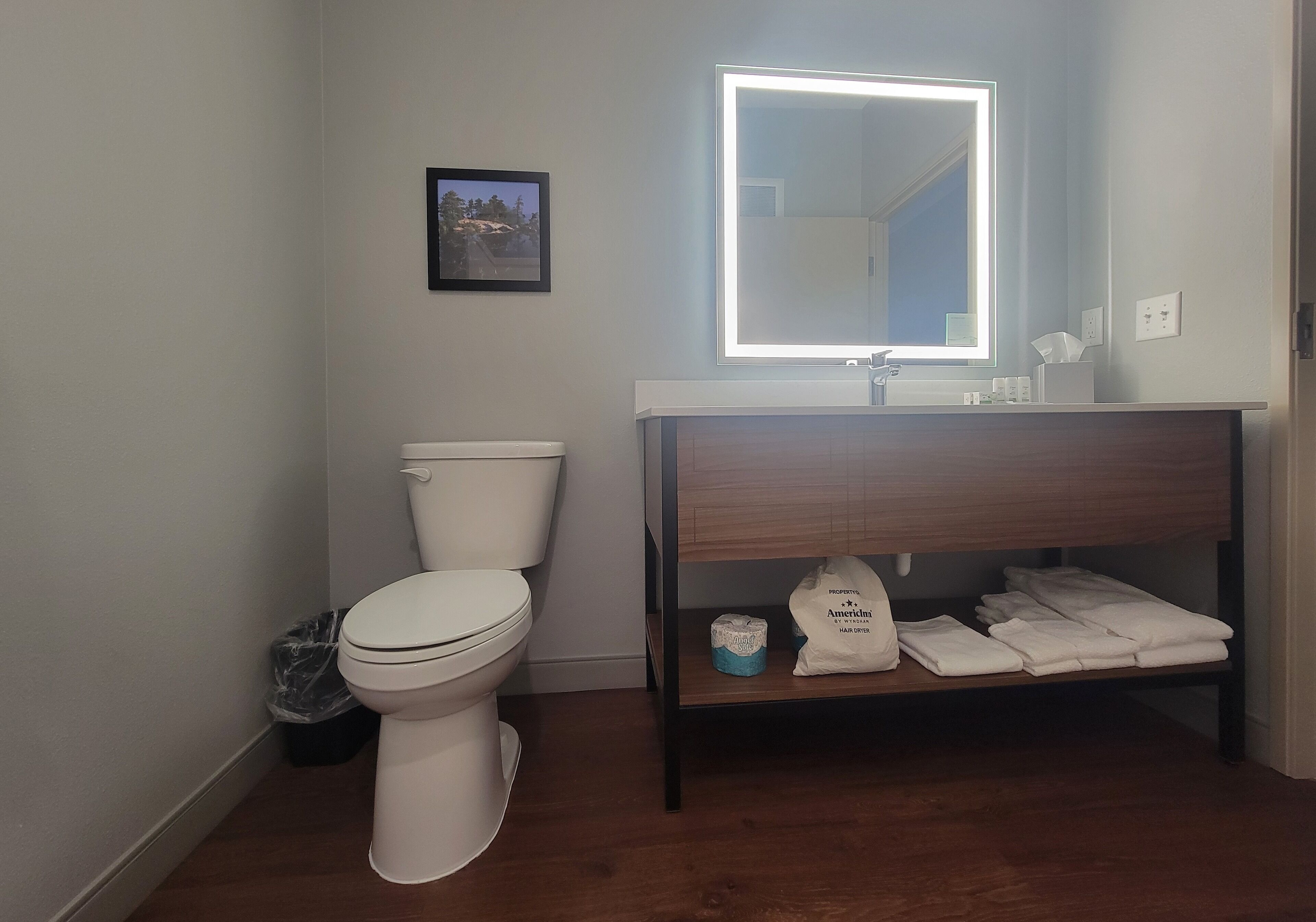 A bathroom with a toilet, a sink with a mirror, and a shelf with towels and toilet paper.