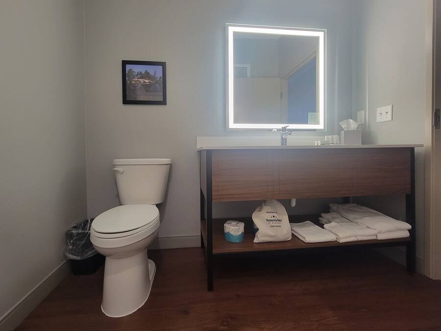A bathroom with a toilet, a sink with a mirror, and a shelf with towels and toilet paper.