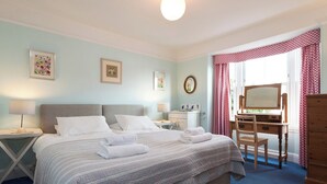 Un dormitorio con cama, mesita de noche, lámpara, cómoda, espejo y escritorio.
