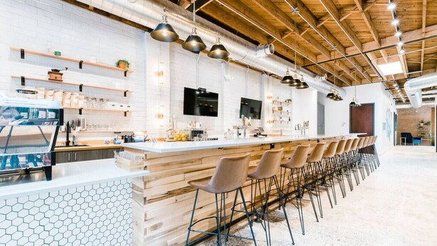 Un área de bar moderna con una barra alargada, varios taburetes y un salpicadero de azulejos hexagonales blancos.