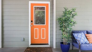 Puerta principal con un panel de vidrio, una planta en maceta y un sofá azul con cojines estampados.