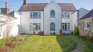 A two-story house with a white exterior, a stone chimney, and a well-maintained lawn with a stone pathway leading to the front door. - 3 bedroom accommodation in Clynnog Fawr (Clynnog Fawr)