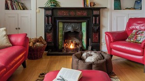 A cozy living room with a fireplace, red leather chairs, a dog bed, and a bookshelf filled with books. - 3 bedroom accommodation in Clynnog Fawr (Clynnog Fawr)