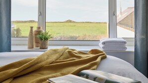 A bedroom with a bed, a window with a view of a green field, and a stack of white towels. - 3 bedroom accommodation in Clynnog Fawr (Clynnog Fawr)