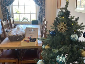 Un árbol de Navidad con adornos, un letrero de bienvenida, una cesta con objetos y una ventana con cortinas.