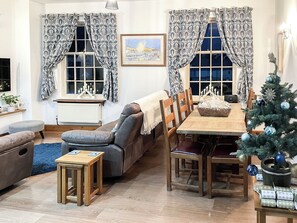 Una sala de estar acogedora con un sofá, una mesa de comedor con sillas, una mesita de madera y un árbol de Navidad.