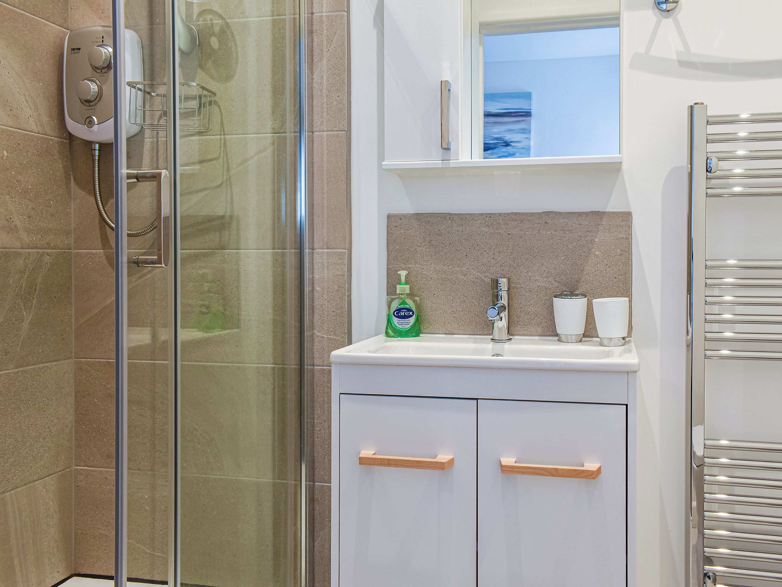 Een badkamer met een douchecabine van glas, een witte wastafel met een spiegel erboven en een handdoekrek aan de rechterkant.